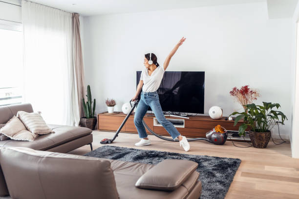 A woman vacuums the living room while energetically dancing, illustrating a quick yet fun cleaning routine.