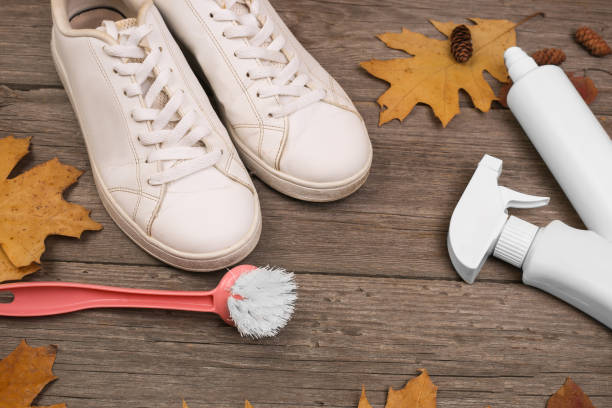 White shoes with cleaning supplies and autumn leaves on a wooden surface, ready to be cleaned.